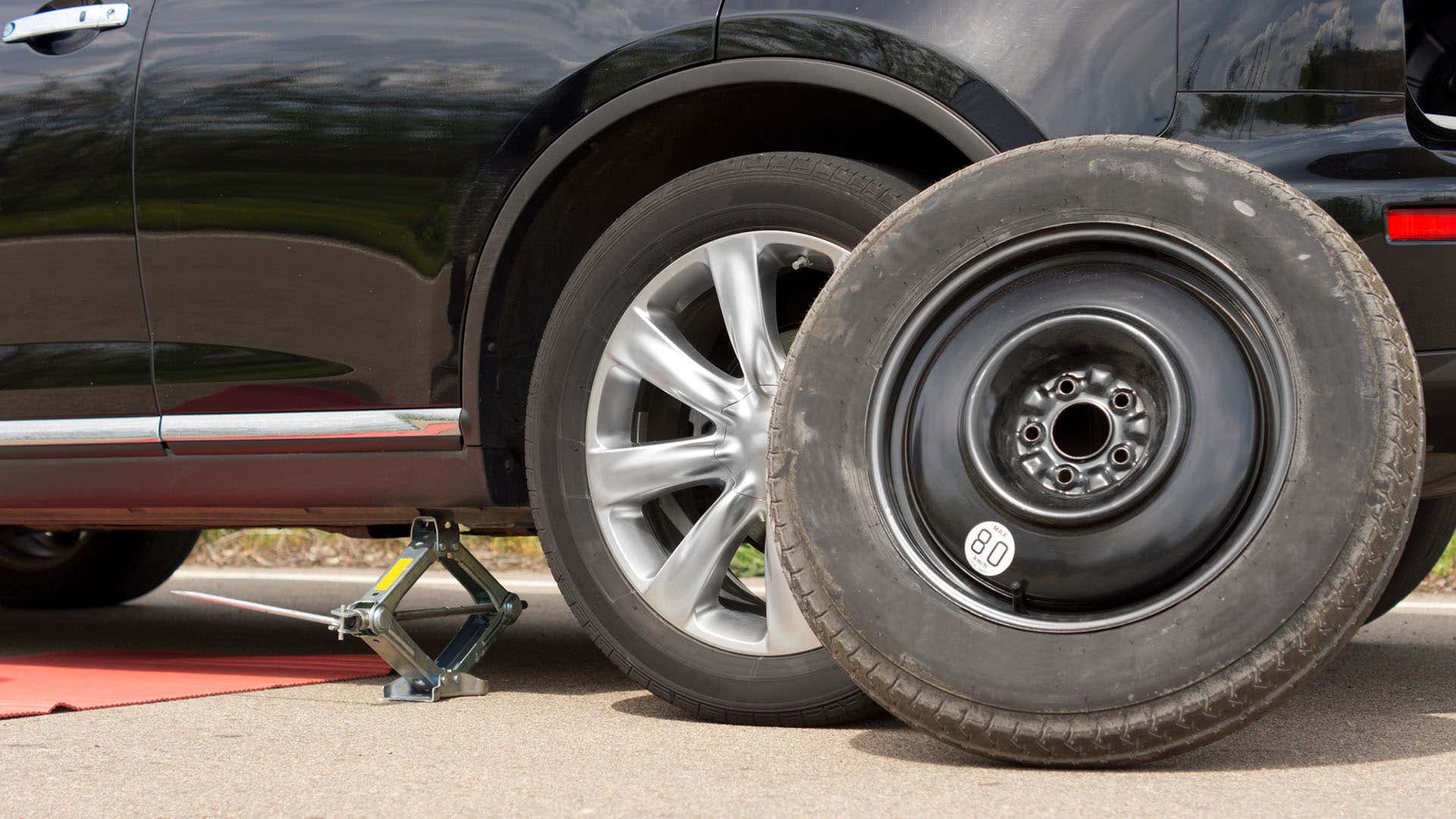 一个漏气的轮胎放在一辆被顶起的汽车旁边。