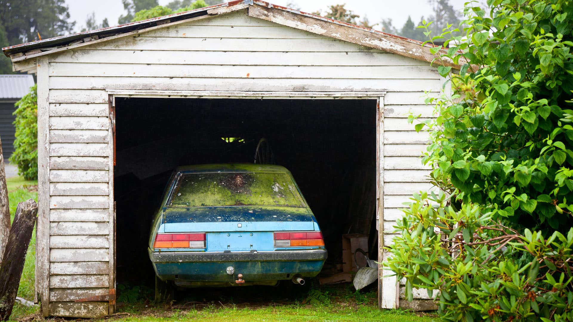 一辆被放弃的欧洲汽车在一个小车库中看到有磨损的白色油漆。