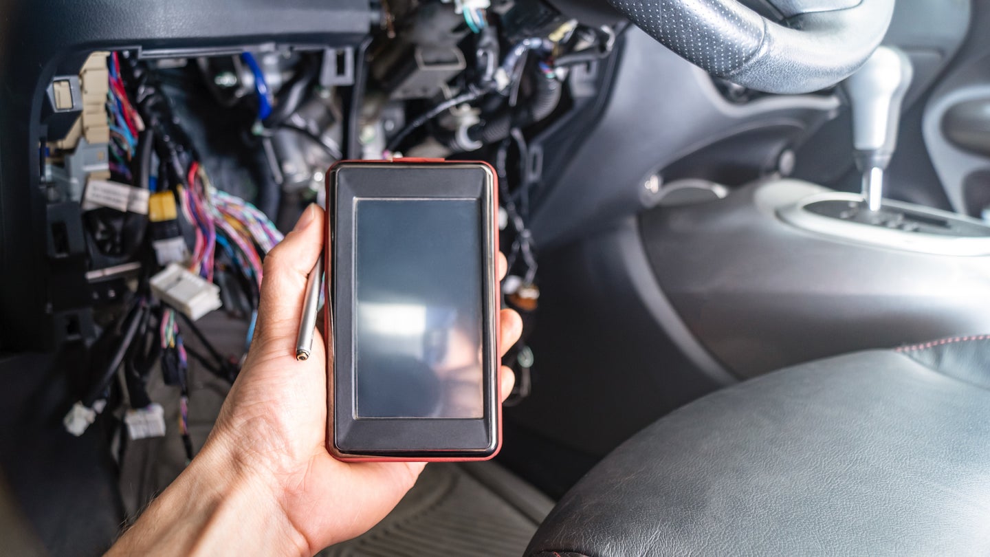 汽车故障诊断：电工手中的带OBD2接口的便携式自动扫描仪。在汽车的内部的背景与拆除的面板和电线。